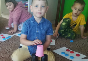 Chłopiec zbudował na dywanie wieże z plastikowych kubków